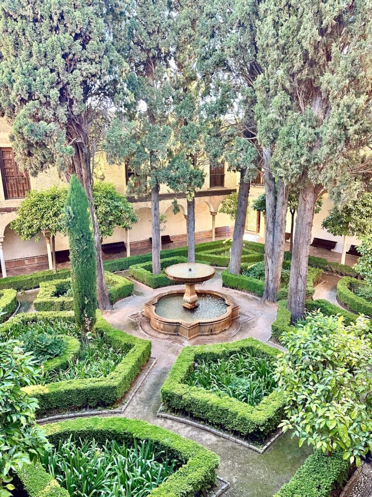 An inner courtyard of the Alhambra's Nasrid Palaces with decorative boxwood hedges.