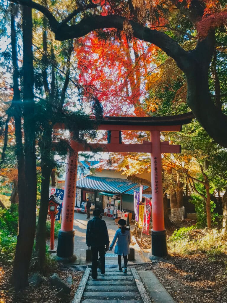Brilliant orange and red autumn foliage around the final torii gate before the exit of the trail at Mount Inari