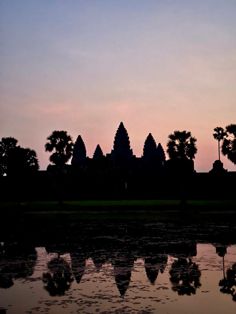 A pink glow lights up the sky shortly before sunrise at Angkor Wat