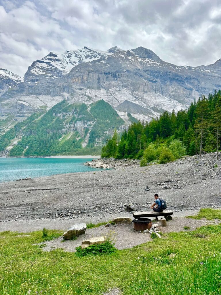 A person sitting on a bench on the rocky beach at Oeschinen Lake