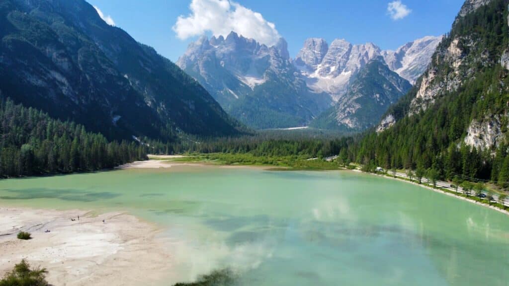 Aqua green waters of lago di dobbiaco in front of snow capped mountains just a short drive from Cortina
