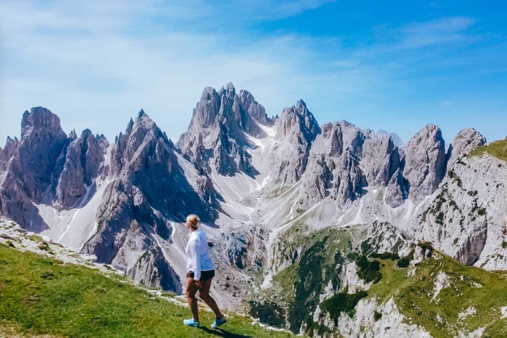 Woman walking across a green alpine meadow with the dramatic Cadini di Misurina spires rising behind her in the Italian Dolomites