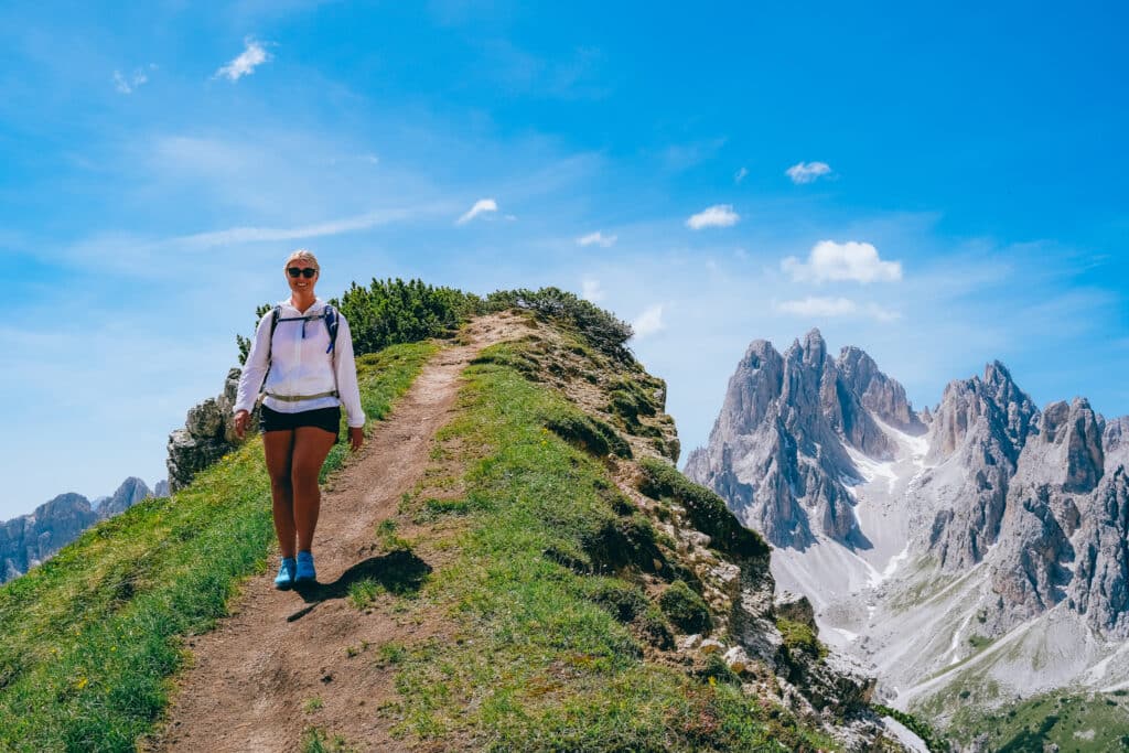 Woman walking the grassy ridge trail at Cadini di Misurina with the limestone spires rising to the right in the Italian Dolomites