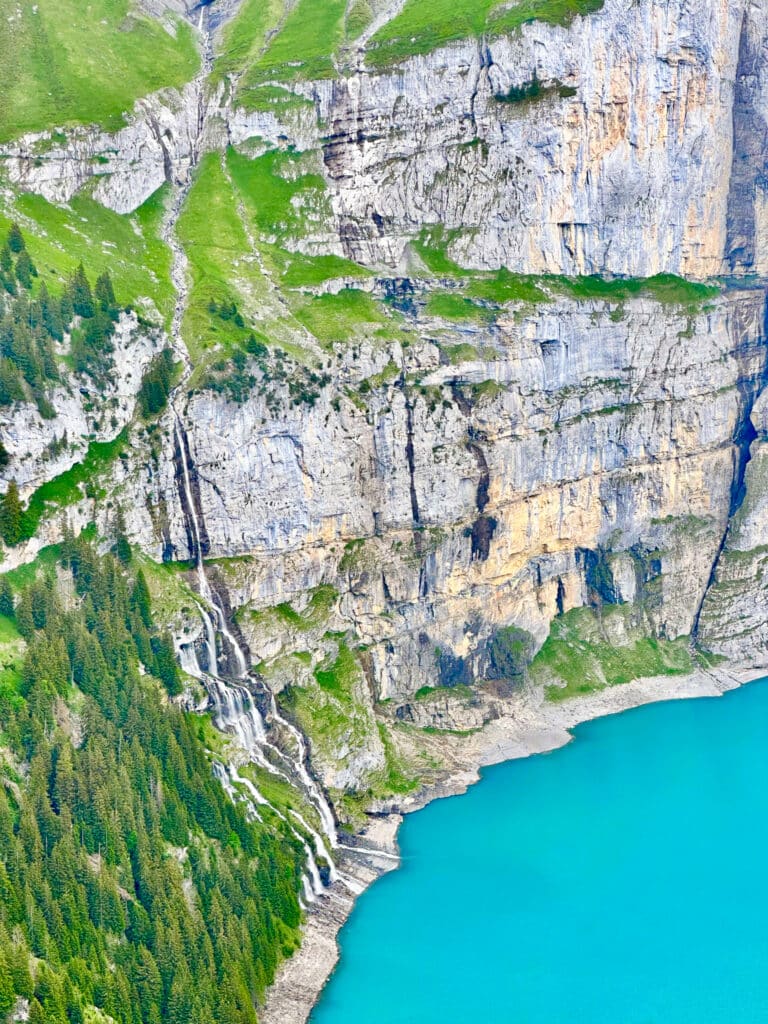 Aerial view of waterfalls cascading down a sheer cliff face into the turquoise waters of Oeschinensee, Switzerland
