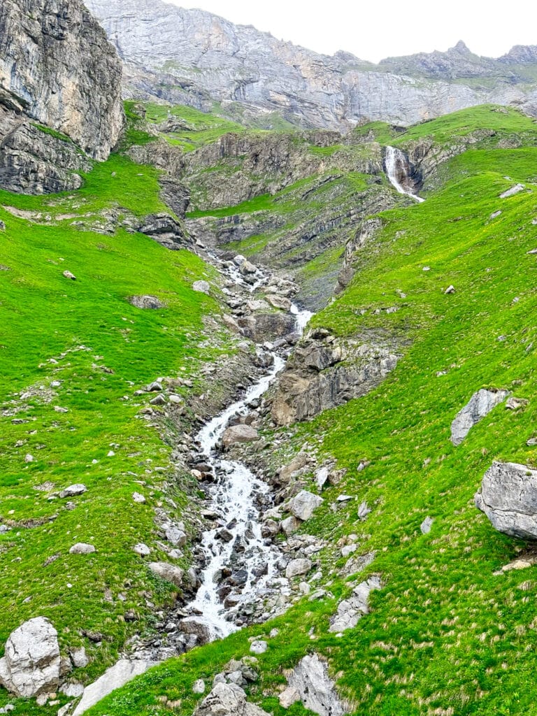A narrow glacial stream tumbling over rocks down a steep green hillside above Oeschinensee, Switzerland
