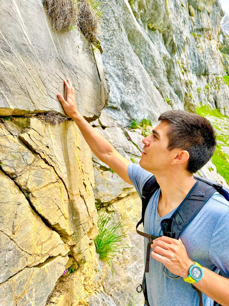 Male hiker touching and examining the surface of a smooth rock face on the Oeschinensee trail, Switzerland