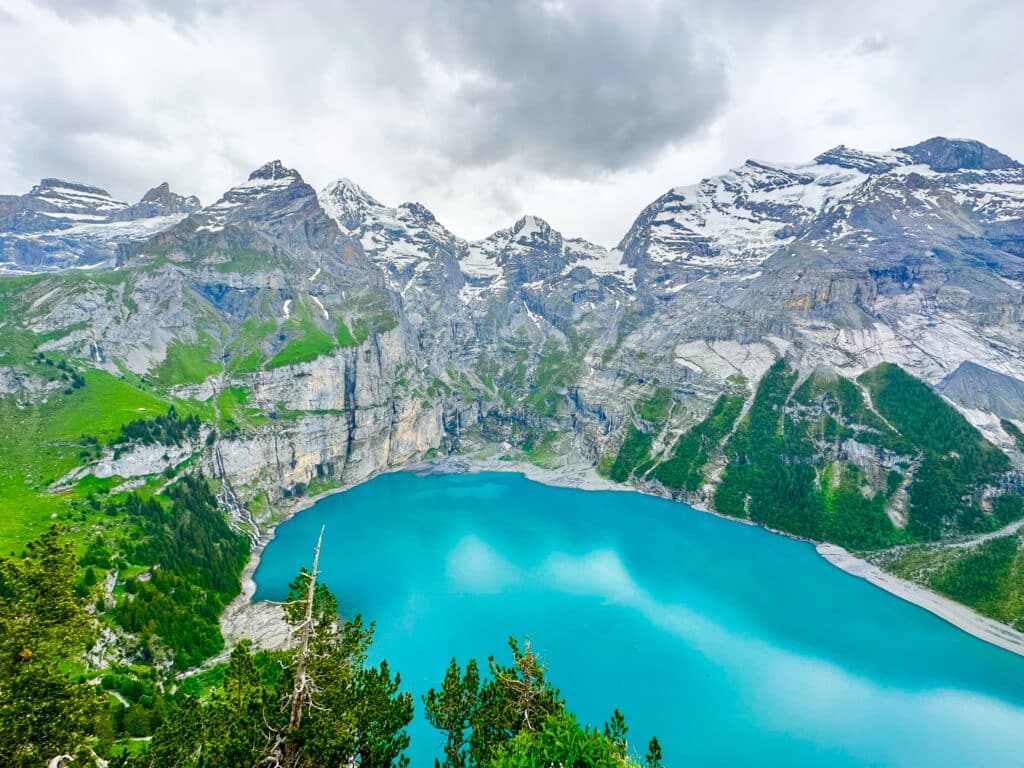 Wide-angle view of the full Oeschinensee lake from above, framed by glacier-topped mountains in the Bernese Oberland