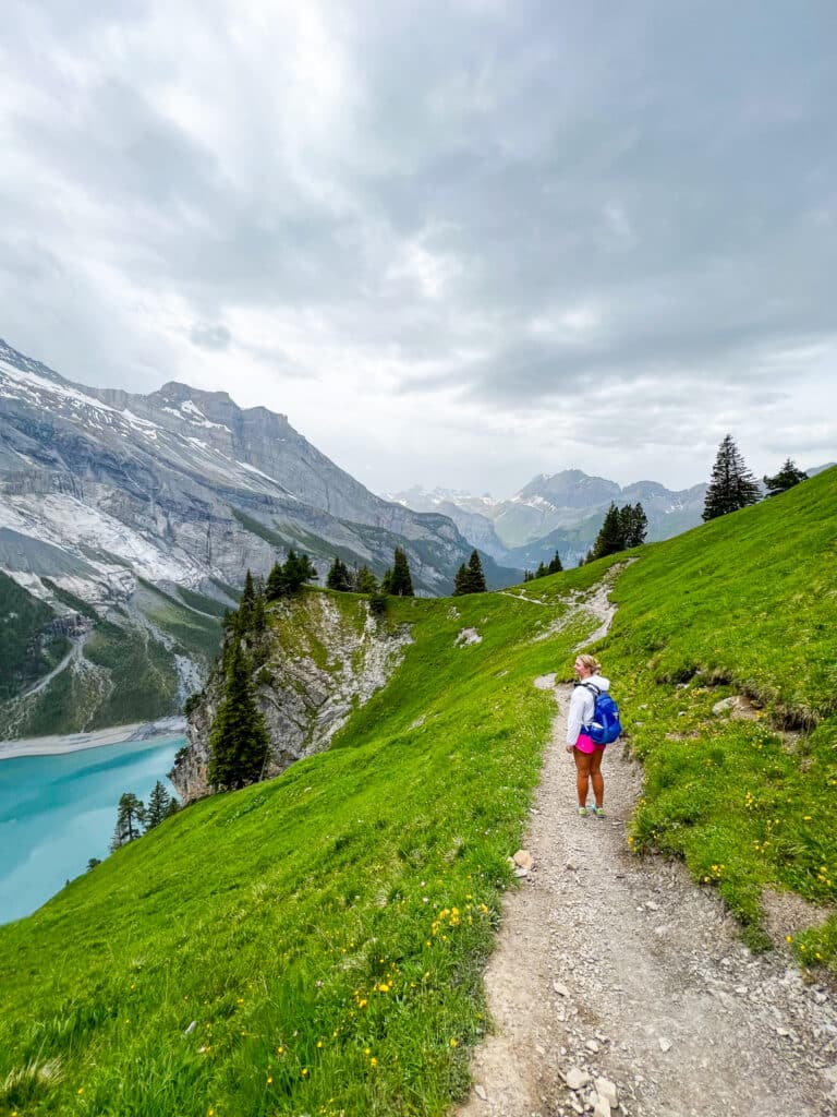oman hiking on the Oeschinensee trail with the turquoise lake glinting below on the left and green meadows ahead
