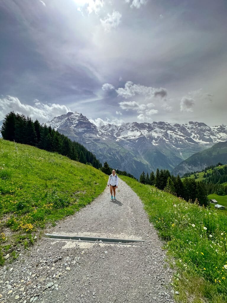Female hiker on a wide alpine path with dramatic clouds gathering over snow-capped peaks above Mürren, Switzerland