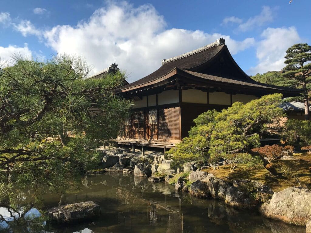 View of Tenryu-ji Temple in Arashiyama, Kyoto, reflected in a tranquil pond and surrounded by carefully manicured pines and traditional gardens.