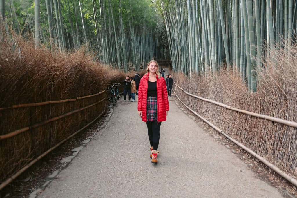 "Woman walking down the central path of Arashiyama Bamboo Forest in Kyoto, surrounded by tall bamboo and winter brush on a quiet morning."