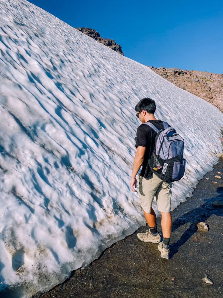 Hiker walking alongside a snowbank with ice melt running across the trail on Skyline Loop