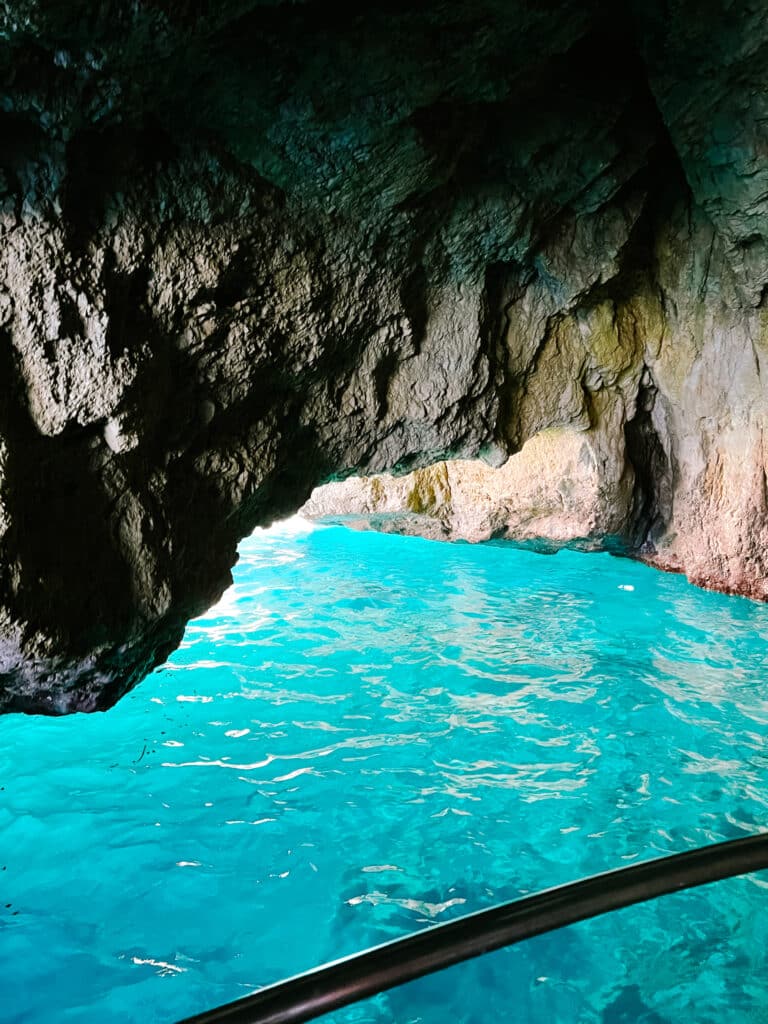 Inside the Green Grotto, a sea cave on Capri, with ethereal turquoise light glowing from the water below and reflecting off the dark rocky cavern walls.
