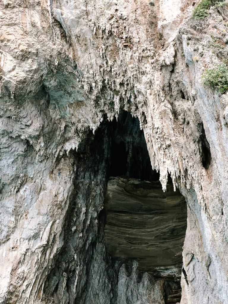 Close-up of a natural cave entrance in Capri's limestone cliffs, revealing textured stalactites hanging from the weathered rock face of the Grotta Bianca