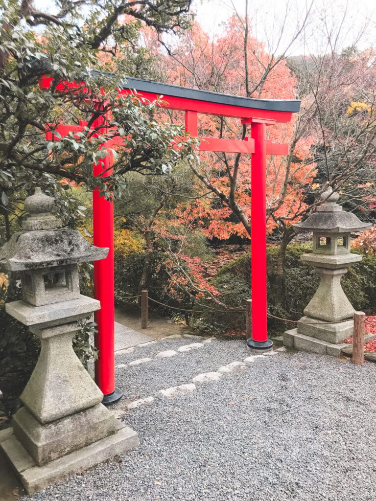 A bright red torii gate, flanked by stone lanterns in the garden of Ryoanji Temple in Kyoto, Japan
