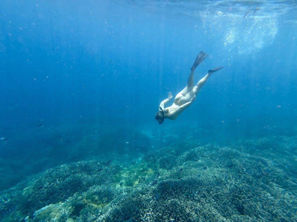 A snorkeler floating over a reef with clear turquoise water and coral visible below