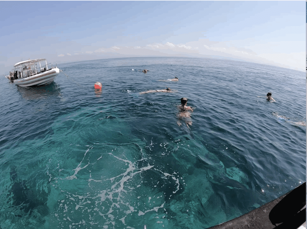 Small wooden snorkel boat anchored in calm turquoise water with swimmers entering the sea near Nusa Penida.