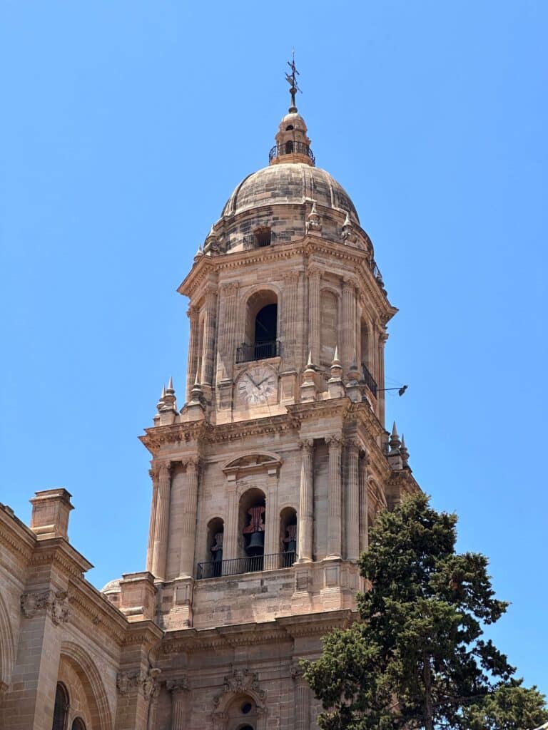 Bell tower of the Málaga Cathedral against a clear blue sky.