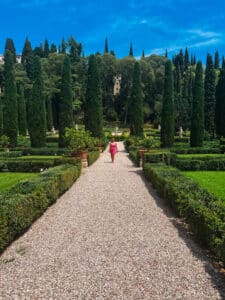 Gravel pathway through Giardino Giusti, flanked by box hedges and towering cypress trees under a vivid blue sky.