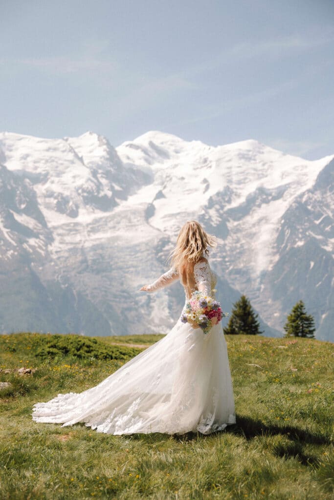 Bride in a long train gown looking out toward Mont Blanc from a grassy alpine meadow. Photo credit: Mathilde Rietsch