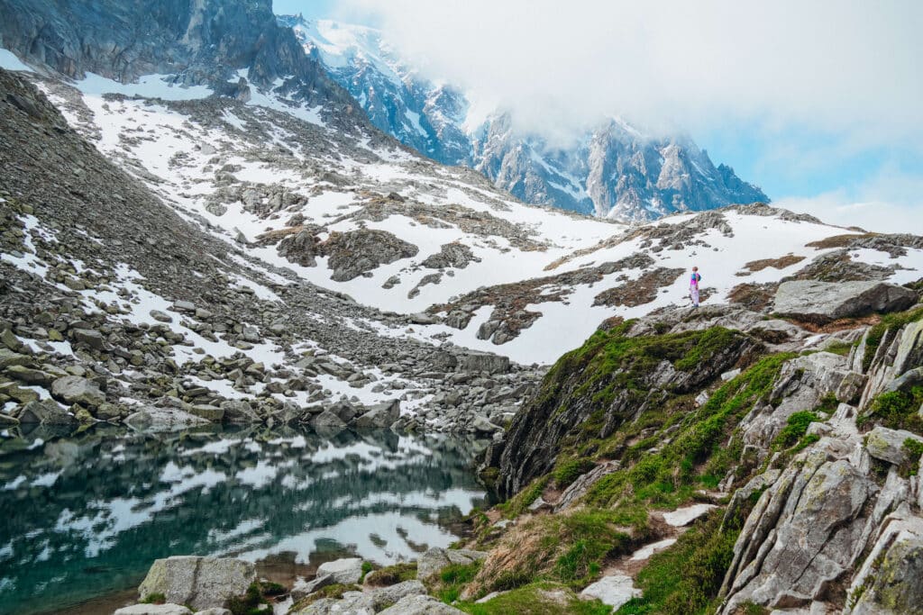 Hiker standing at the edge of Lac Bleu, gazing at the still, reflective water and misty mountains.