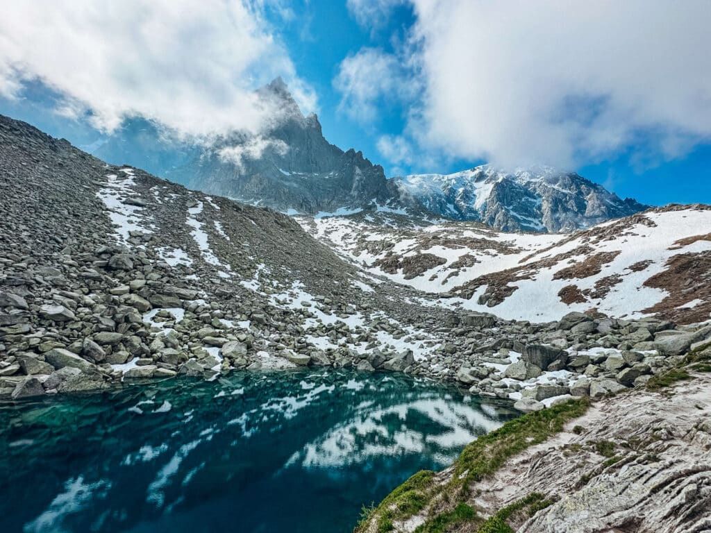 View of Lac Bleu reflecting jagged peaks and snowfields under a moody sky.