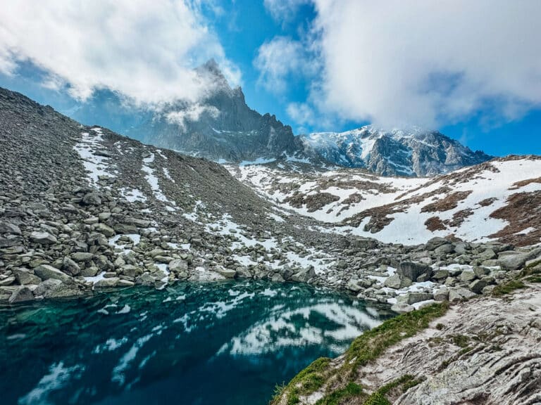 View of Lac Bleu reflecting jagged peaks and snowfields under a moody sky.