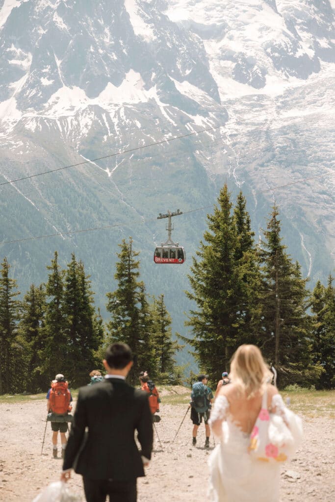 Bride and groom walking hand-in-hand toward the gondola lift at Brévent with Mont Blanc ahead. Photo credit: Mathilde Rietsch
