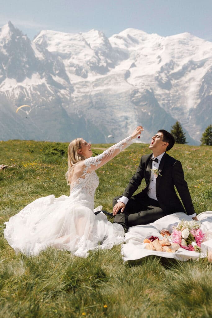 Couple enjoying a picnic in wedding attire on a sunny alpine meadow with Mont Blanc in the background. Photo credit: Mathilde Rietsch