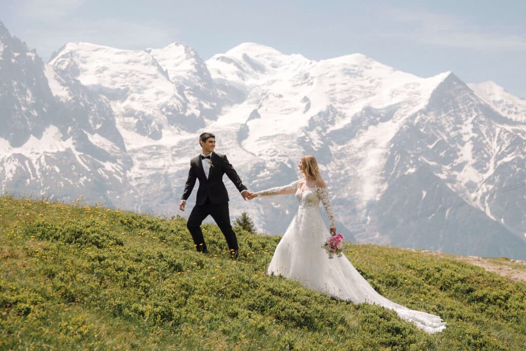 Bride and groom running hand-in-hand across a meadow near Planpraz with sweeping Alpine views. Photo credit: Mathilde Rietsch.