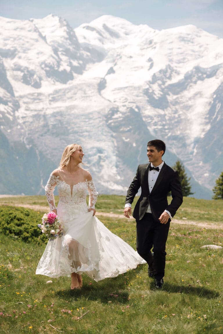 Newlyweds running joyfully across the meadow at Planpraz, with sweeping views of the Alps. Photo credit: Mathilde Rietsch