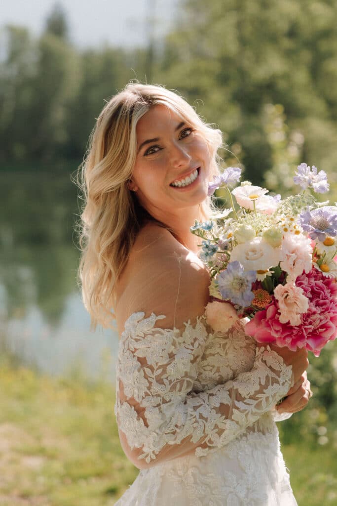 Bride holding a colorful wildflower-style bouquet by Fleuri'Cimes, smiling softly. Photo credit: Mathilde Rietsch.