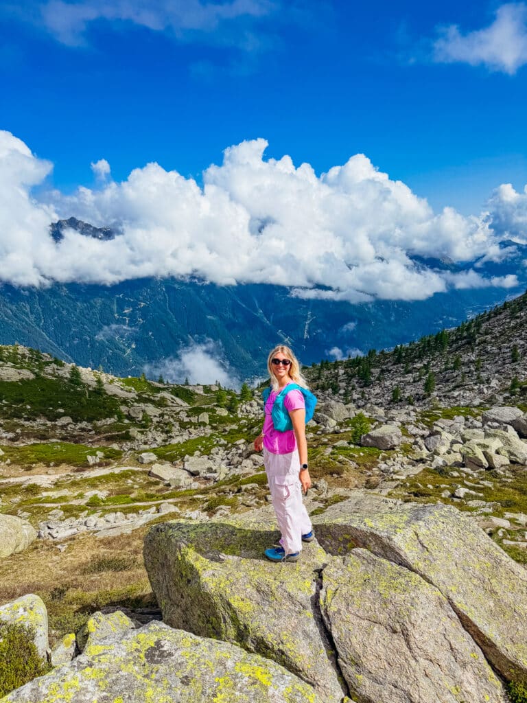 A happy hiker in pink pants perched on a lichen covered rock on the Grand Balcon Nord hike, one of the best hikes in Chamonix