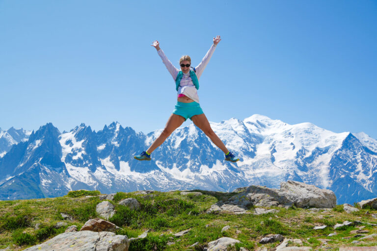 Woman jumping for joy in front of Mont Blanc after saving money with the Mont Blanc MultiPass, summer hiking near a Chamonix lift-accessed trail
