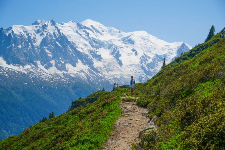 Trail runner on a narrow trail carved along mountainside with glacier and peaks ahead