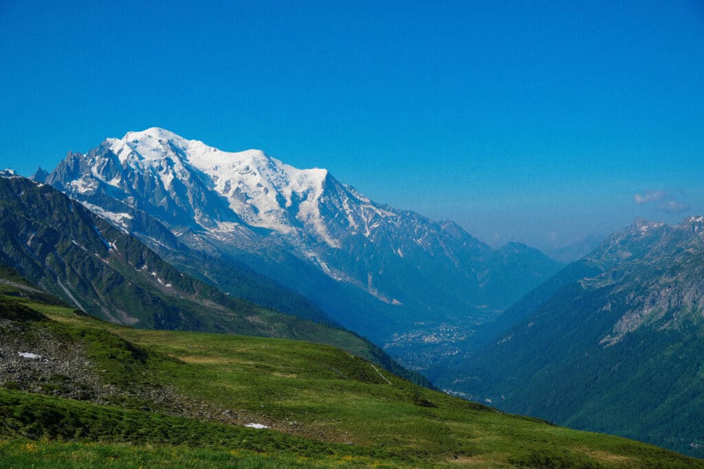 Panoramic view of the Chamonix valley with snow-covered peaks rising behind grassy alpine slopes.