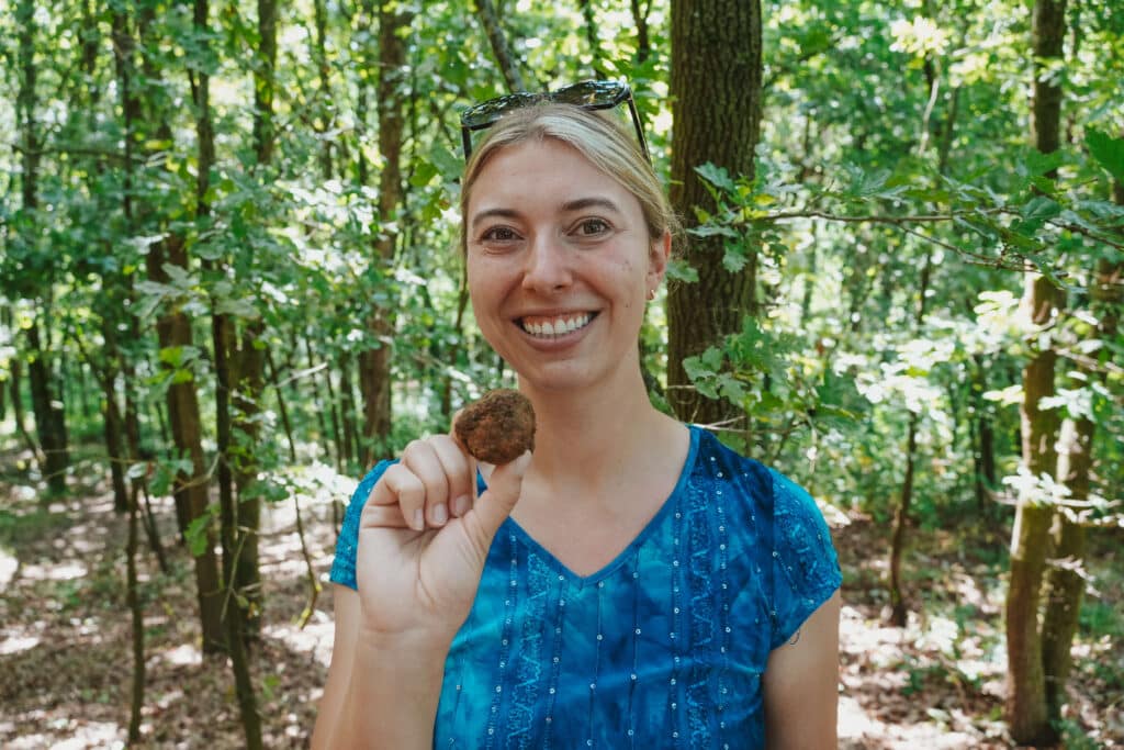 Smiling woman holding up a freshly found black truffle in a sunny forest clearing in the forests 45 minutes from Turin