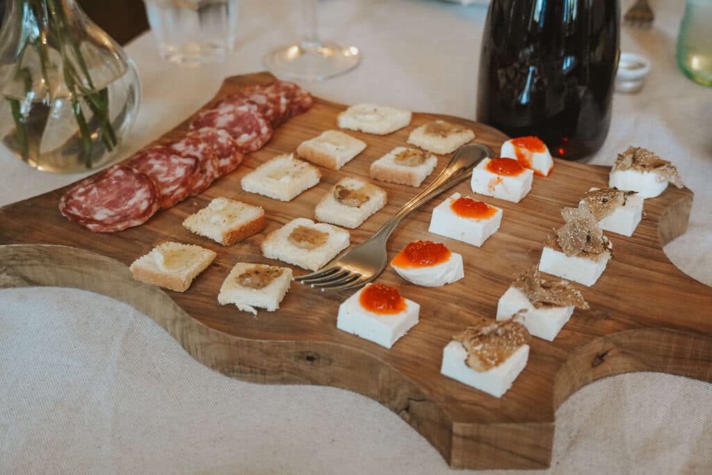 A wooden cutting board with neat rows of local sausage slices, and fresh cheese topped with fresh black truffle shaving, jams, and tapenades