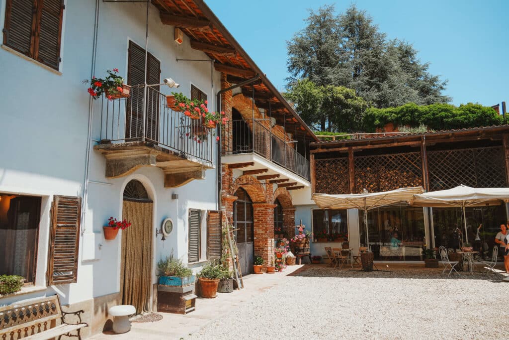 Exterior of Aloi Luca agriturismo, with flower boxes overflowing with bright pink flowers, rustic whitewashed walls, and a sunny courtyard