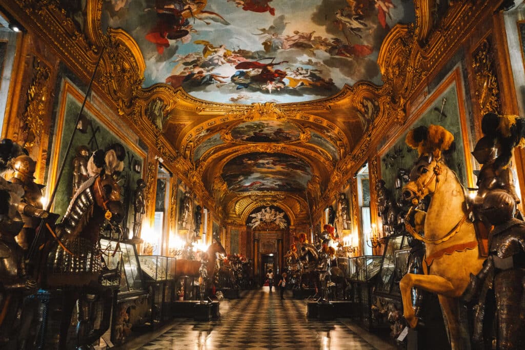 Lavishly decorated hallway lined with suits of armor and frescoed ceilings in the Royal Armory of Turin.