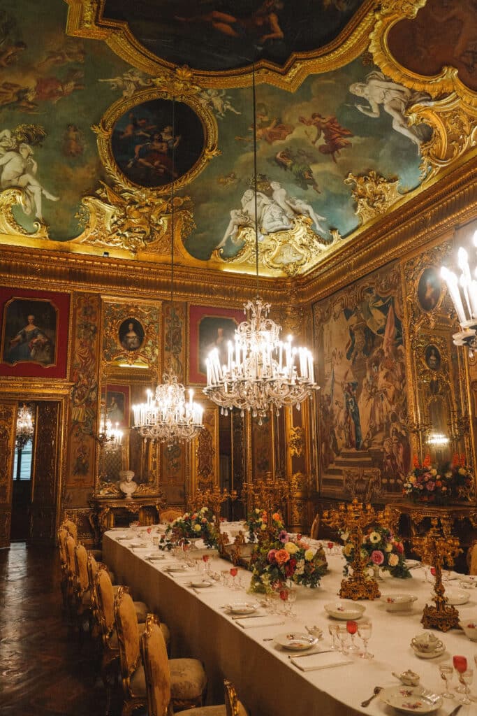 Formal dining room with a long banquet table, floral arrangements, and ornate ceiling paintings in the Royal Palace of Turin.