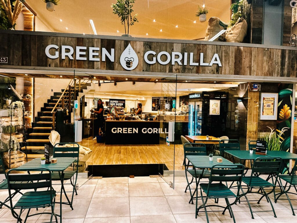 Wide shot of the Green Gorilla Coffee café inside Snell Sports mall in Chamonix, showing green tables and chairs set up in front of a rustic wood storefront.