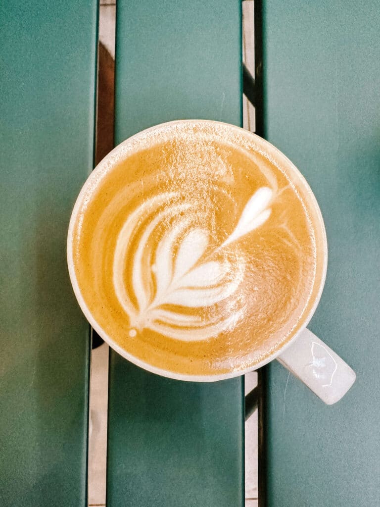 Overhead shot of a cappuccino with latte art on a green metal café table.