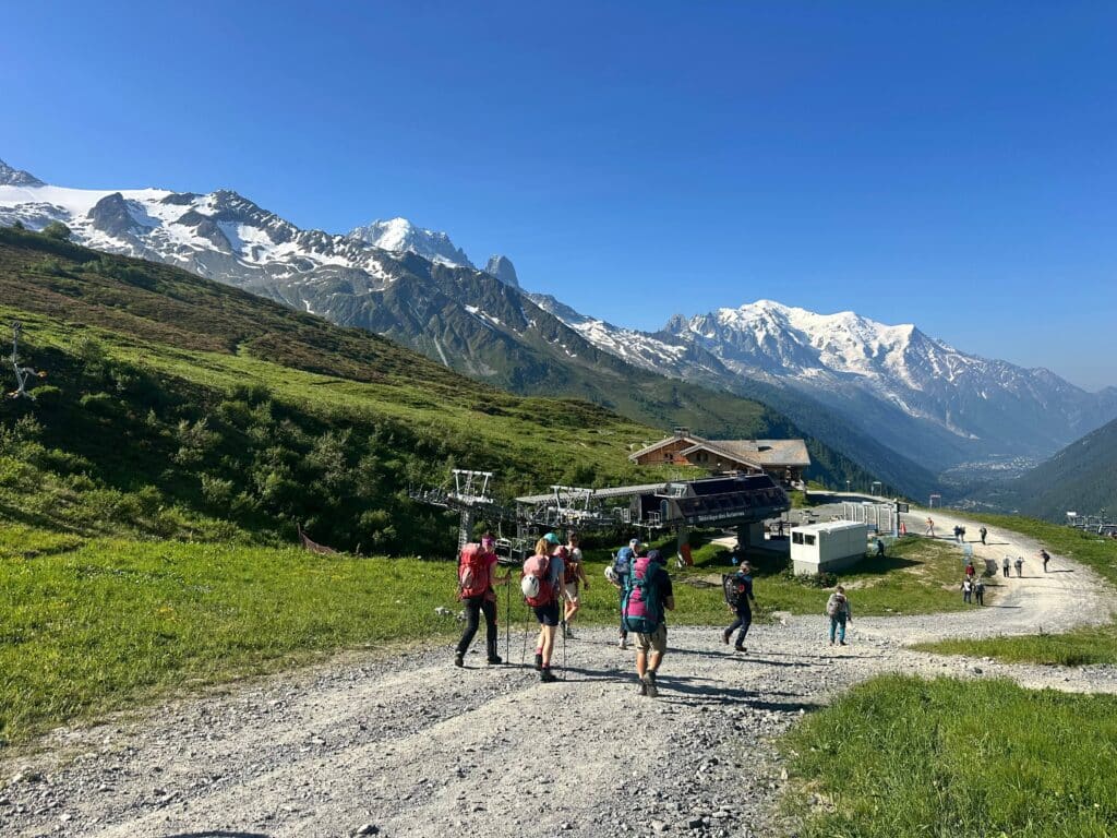 A group of hikers on a gravel track in the mountains above Chamonix under a blue sky.