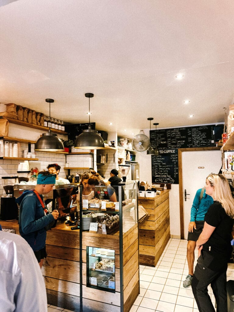 Crowded interior of Moody’s Coffee Roastery showing baristas working behind a wooden counter with hanging lights above.