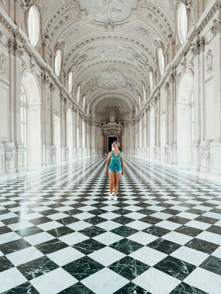 Visitor standing in the center of Venaria’s checkered Grand Gallery, dwarfed by towering arches