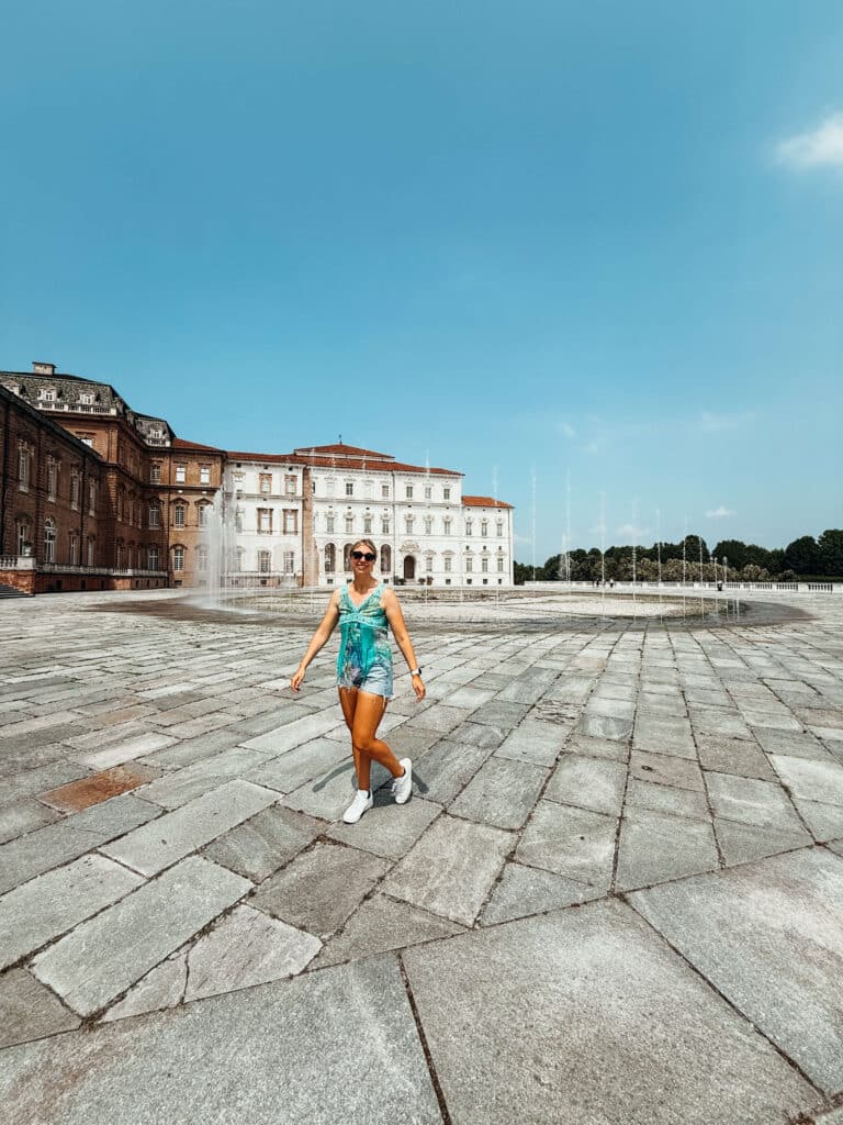 Traveler walking across the vast stone courtyard of the Venaria Reale palace while enjoying the fountain show