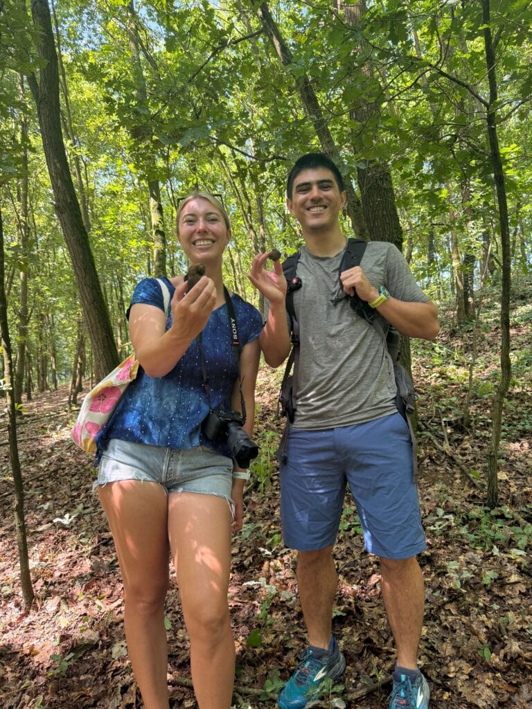 Two people smiling and holding truffles in a forest during a truffle hunting tour.