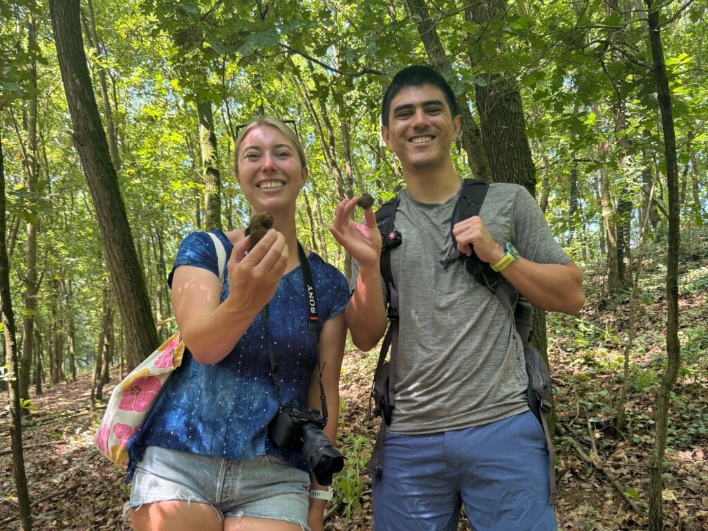 Two people smiling and holding truffles in a forest during a truffle hunting tour.
