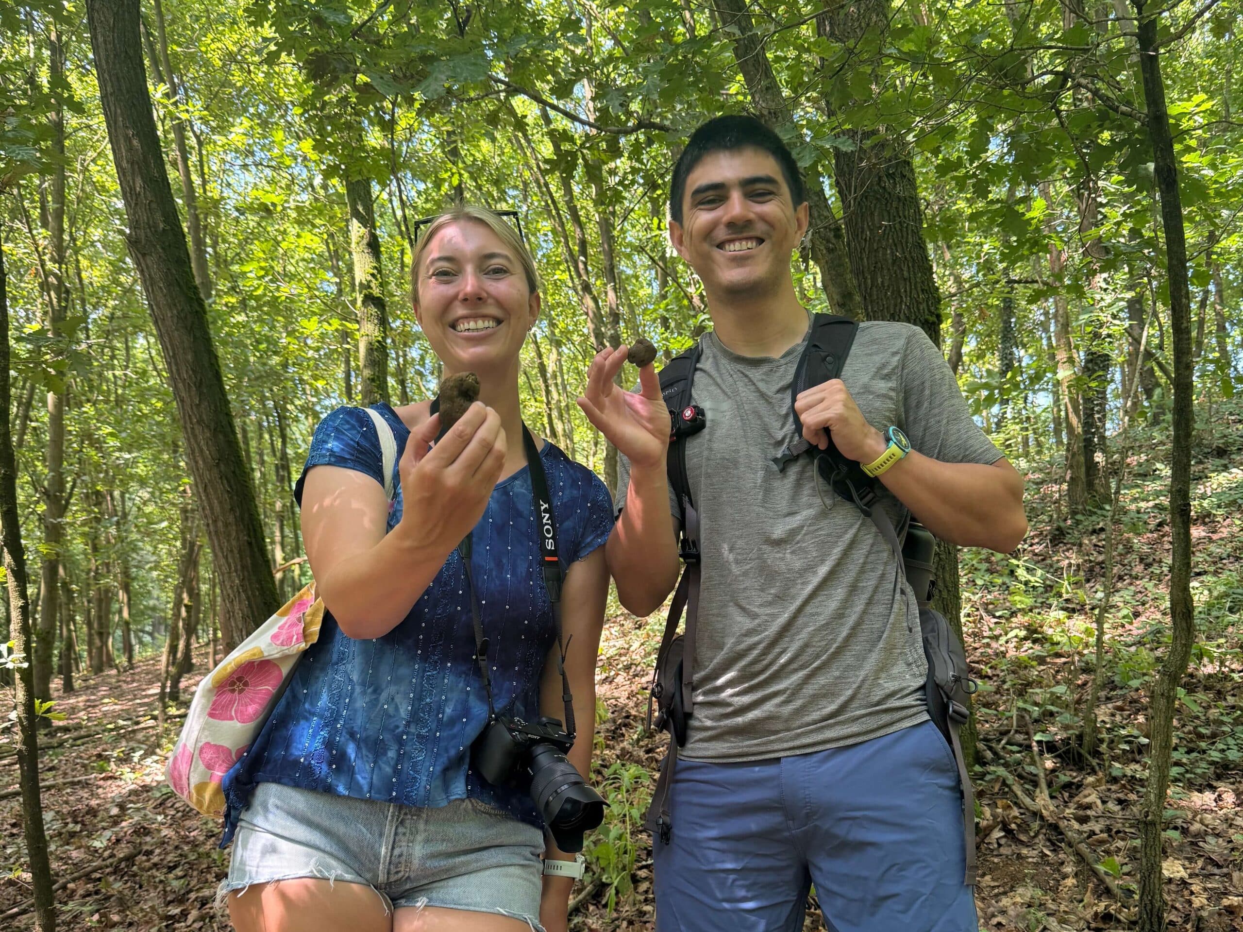 Two people smiling and holding truffles in a forest during a truffle hunting tour.